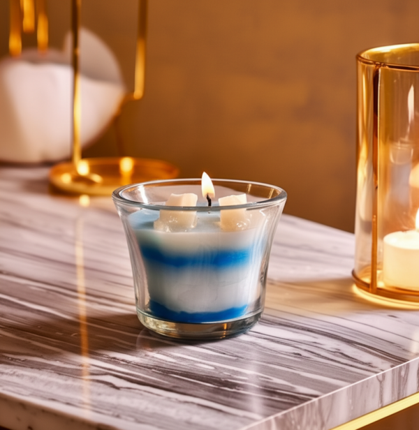 Glass jar scented candle with layered white and blue wax placed on a wooden surface, captured in a cozy indoor setting with natural lighting